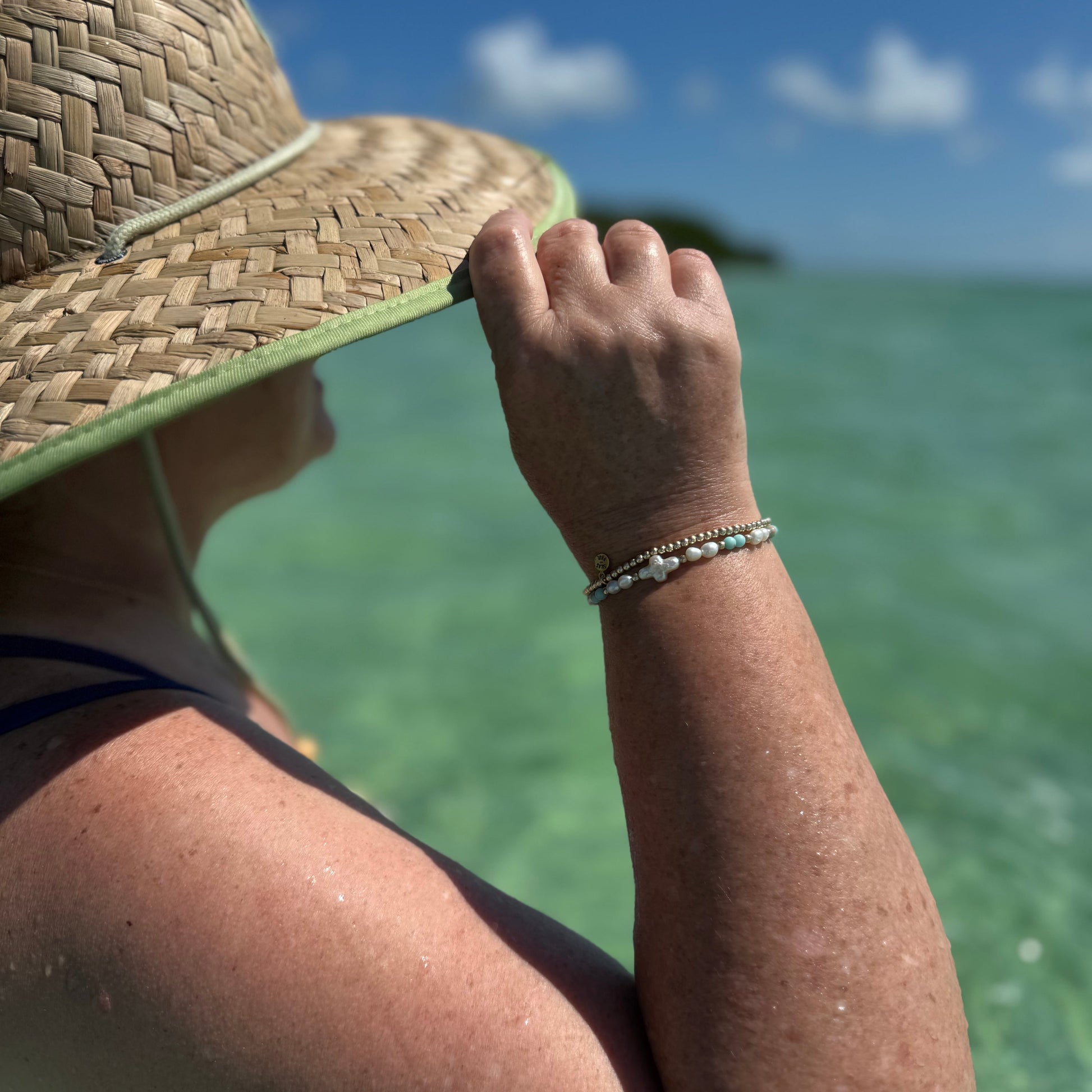 Person wearing a straw hat and bracelets by the water