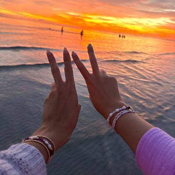 Two hands making a heart shape with a sunset over water in the background