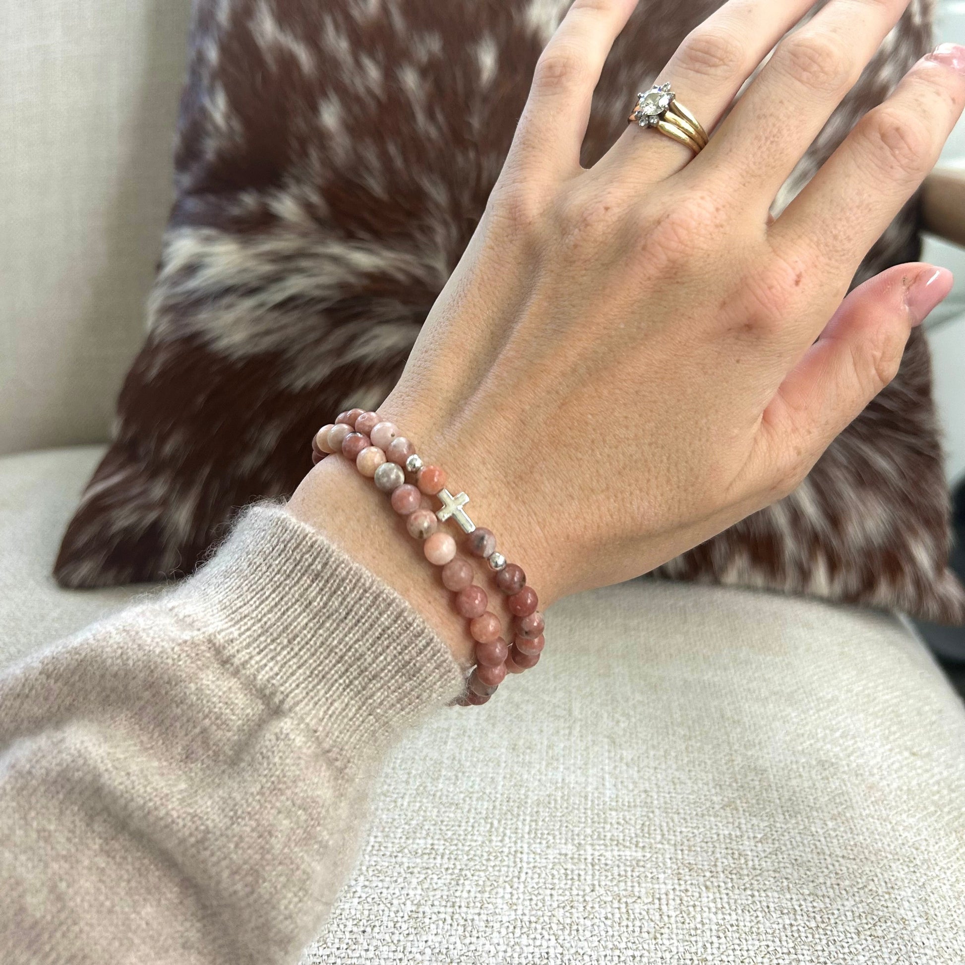 Hand wearing a bracelet and ring on a couch with a cowhide pillow