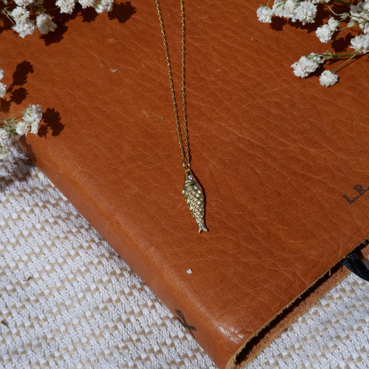 Gold necklace on a brown leather surface with white flowers