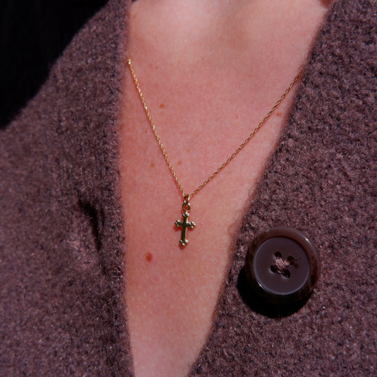 Close-up of a gold necklace with a cross pendant worn by a person in a brown coat.