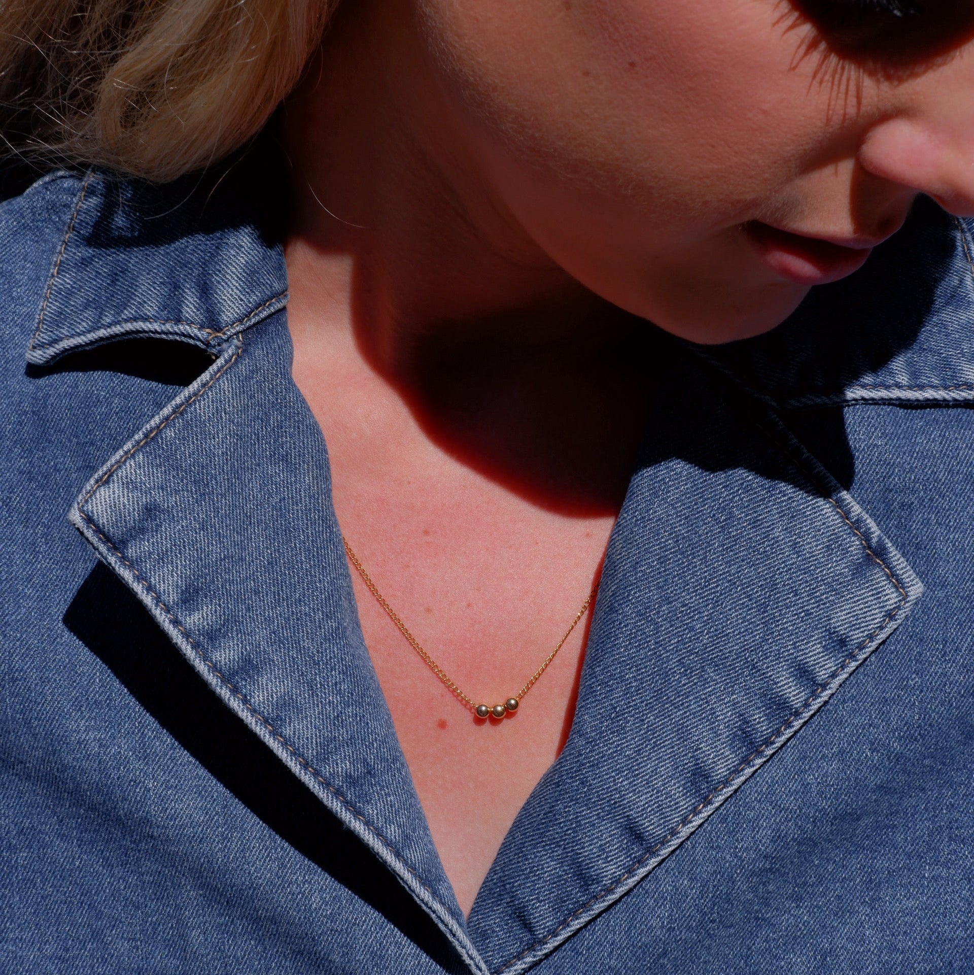 Close-up of a person wearing a blue denim jacket with a necklace.