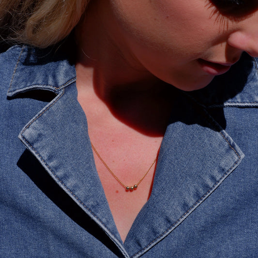Close-up of a person wearing a blue denim jacket with a necklace.