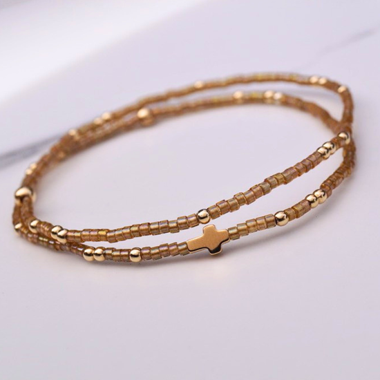 A bracelet set with a gold cross, gold and amber beads, stacked on a marble background.