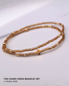 A bracelet set with a gold cross, gold and amber beads, stacked on a marble background.