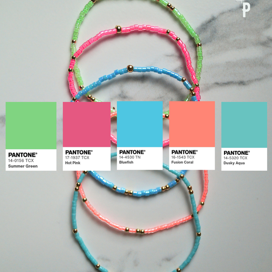 Three beaded bracelets in pink, green, and blue with corresponding Pantone color swatches on a marble background.