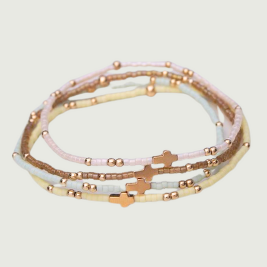 Set of three beaded bracelets with cross charms on a light gray background