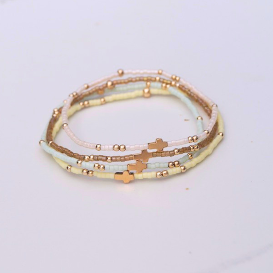 Stack of beaded bracelets with gold cross and accents on a light gray background