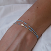 Person wearing a blue beaded bracelet with a cross charm on a white surface