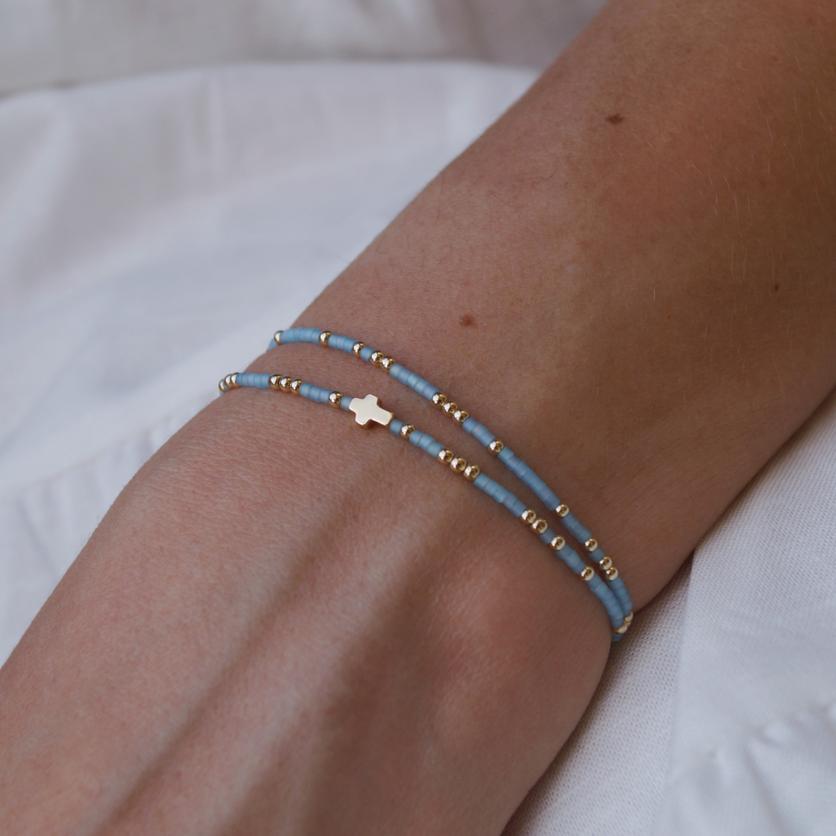 Person wearing a blue beaded bracelet with a cross charm on a white surface