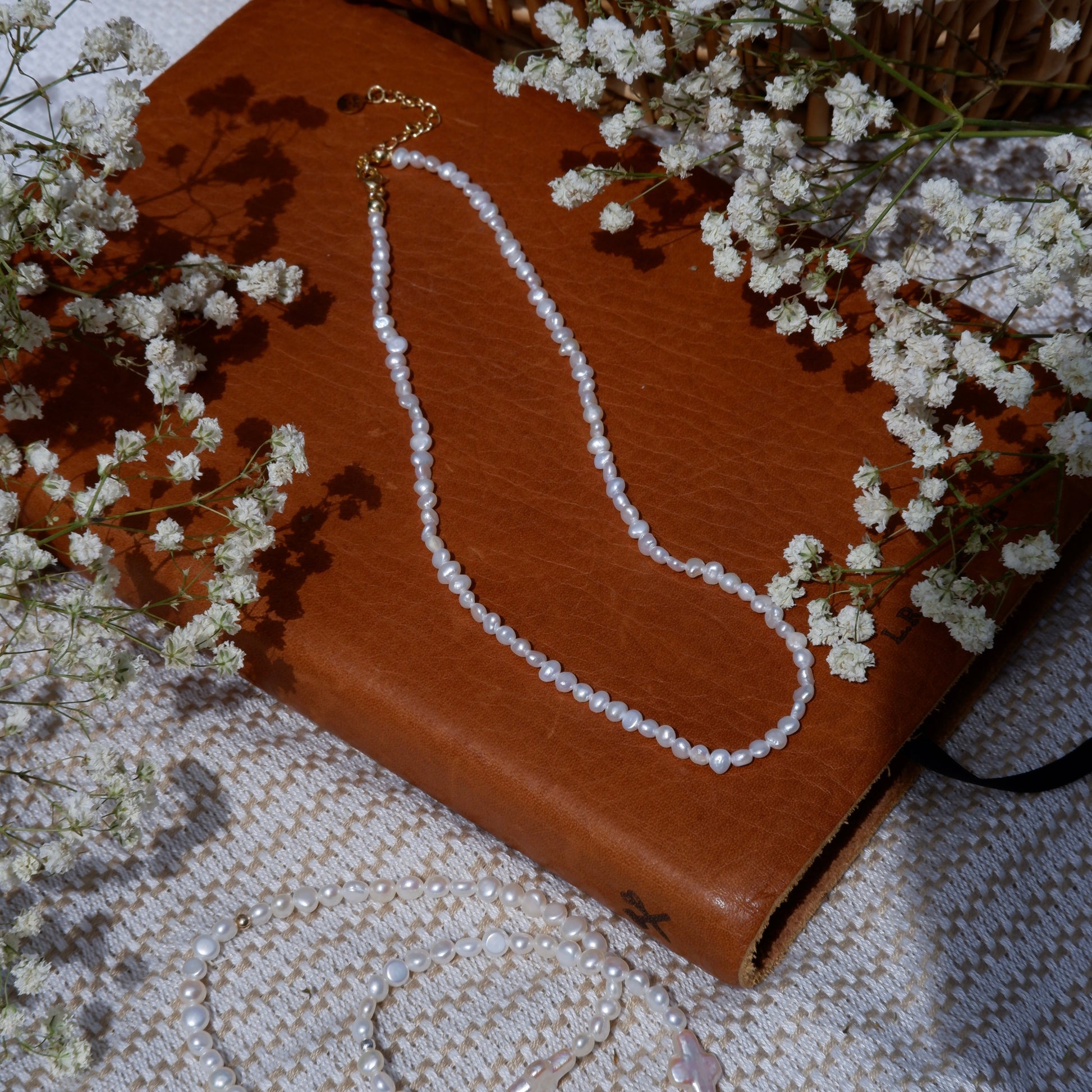 Brown leather wallet with a necklace on a textured surface with small white flowers.