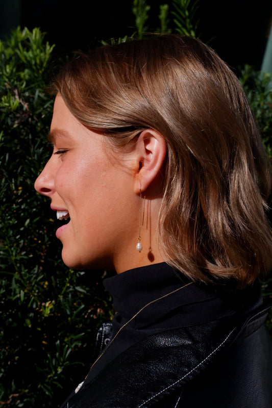 Side profile of a person with short hair and earrings, wearing a black jacket, against a dark background.