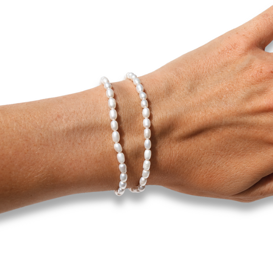 Two white pearl beaded bracelets on a person's wrist, shown against a plain white background with a gold ring visible on the finger.