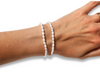 Two white pearl beaded bracelets on a person's wrist, shown against a plain white background with a gold ring visible on the finger.