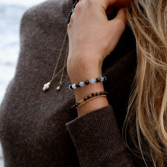 Aquamarine and Bronzite Beaded Bracelet worn stacked with bronzite and gold bracelets by the ocean