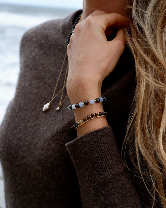 Aquamarine and Bronzite Beaded Bracelet worn stacked with bronzite and gold bracelets by the ocean
